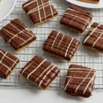 A batch of square chocolate-covered graham crackers with a decorative drizzle of white and dark chocolate placed on a cooling rack.