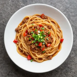 Close-up of a plate of rich, hearty 'Dirty Spaghetti' with a generous amount of sauce, ground meat, and fresh herbs.