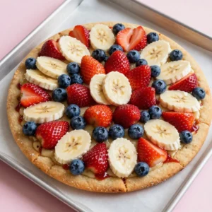 A colorful flag fruit pizza topped with fresh berries and cream cheese frosting, displayed on a wooden table.