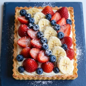 A colorful flag fruit pizza topped with strawberries, blueberries, and bananas arranged in a patriotic design