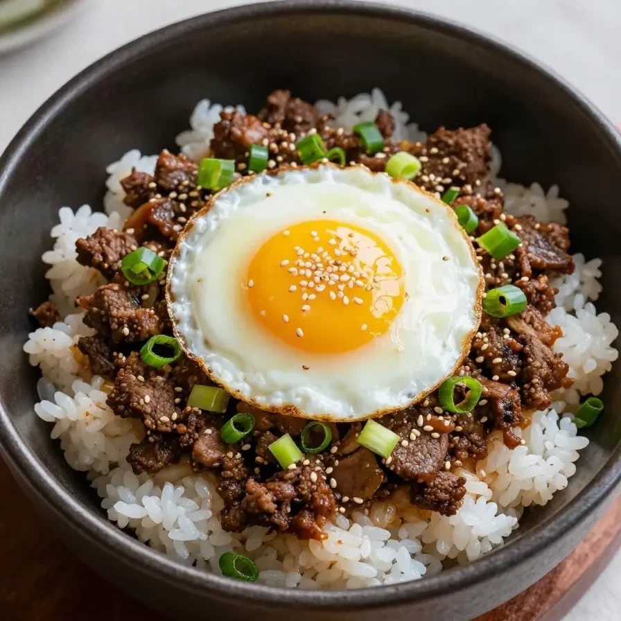 A bowl of Korean ground beef served over white rice, garnished with green onions and sesame seeds.