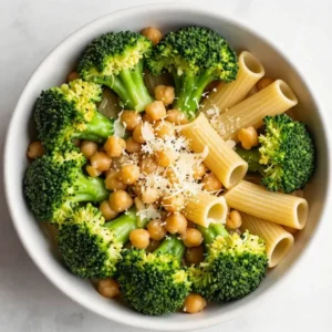A bowl of broccoli chickpea pasta served with fresh parsley on a wooden table.