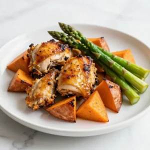 A plate of healthy baked chicken served with roasted sweet potatoes and fresh herbs.